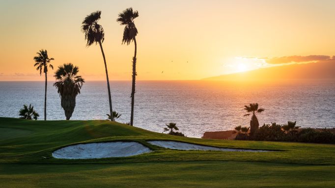 Sunset at Costa Adeje Golf Club with palm trees and a bunker protecting the green
