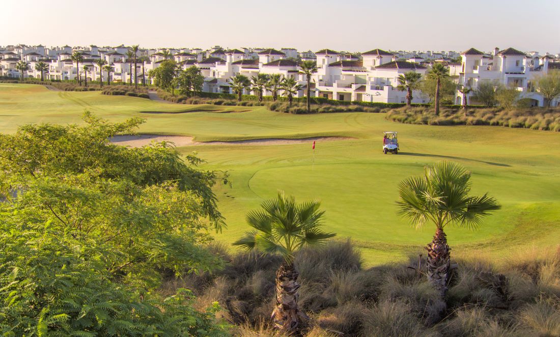 Apartments and villas overlooking green fairway where golfer is in buggy at La Torre