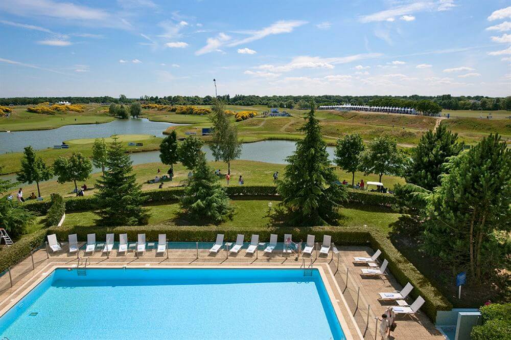 Outdoor swimming pool at Novotel Saint Quentin Golf National with sun loungers and trees with golf course in background