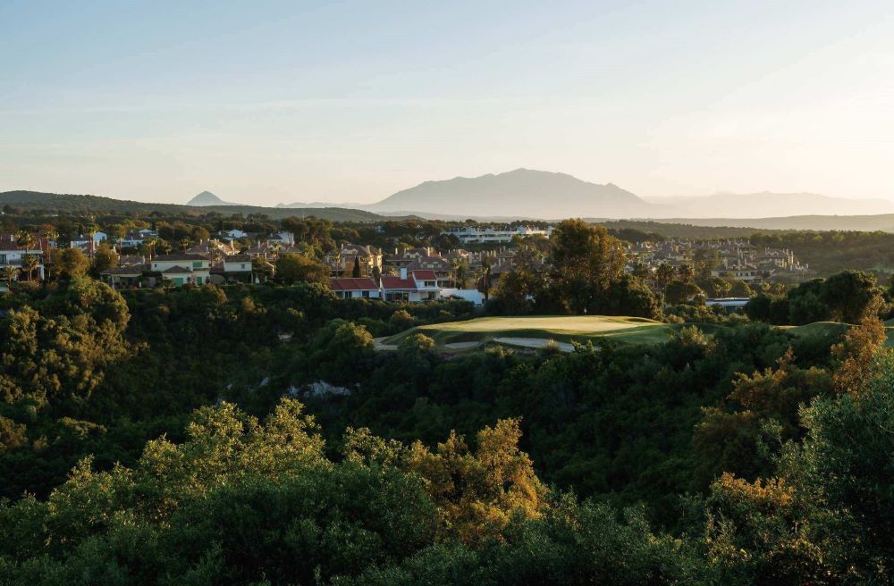 San Roque Golf New Course in Spain with trees surrounding green and houses to the left of the course
