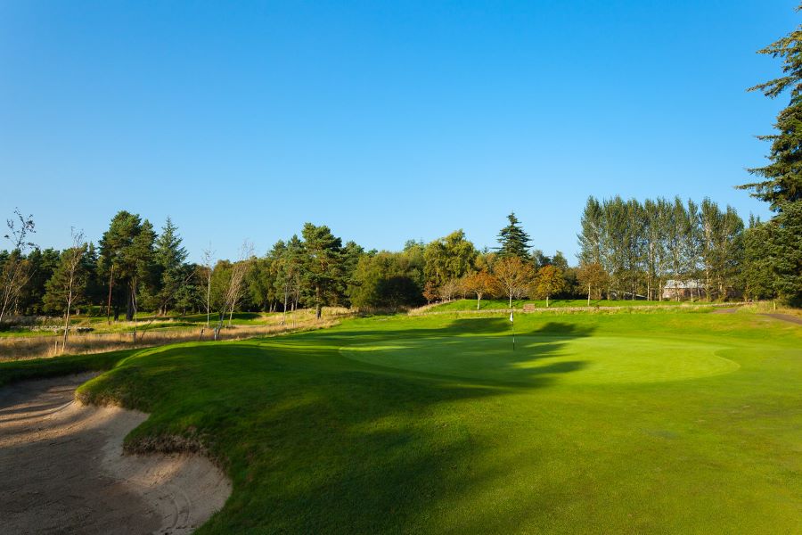 Golf course with lush green grass and edge of sand bunker to the left and blue sky at Slaley Hall Hotel, Spa And Golf Resort