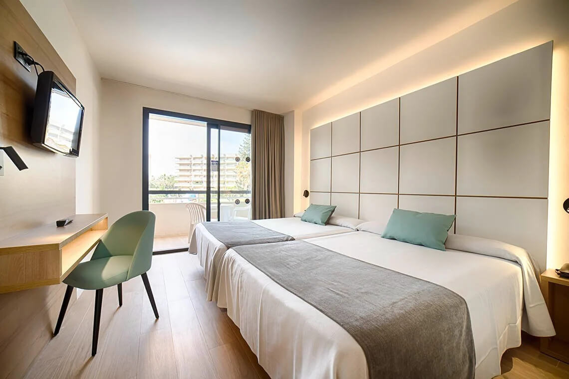 Bedroom at Ohtel Belvedere with television mounted on wall, desk and chair, with patio doors leading to balcony