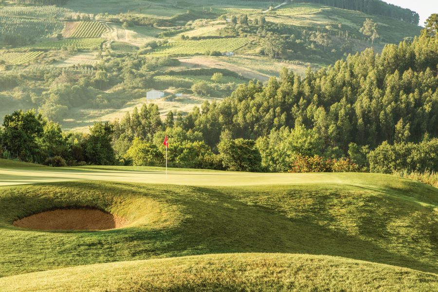 Green trees and countryside on the hills behind this putting green at Dolce by Wyndham CampoReal Lisboa