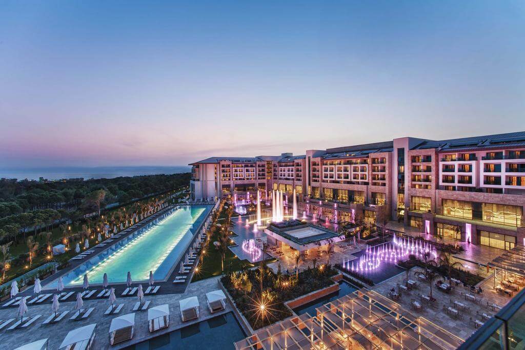 Regnum Carya Golf And Spa Resort at night with views over the swimming pool and sun loungers
