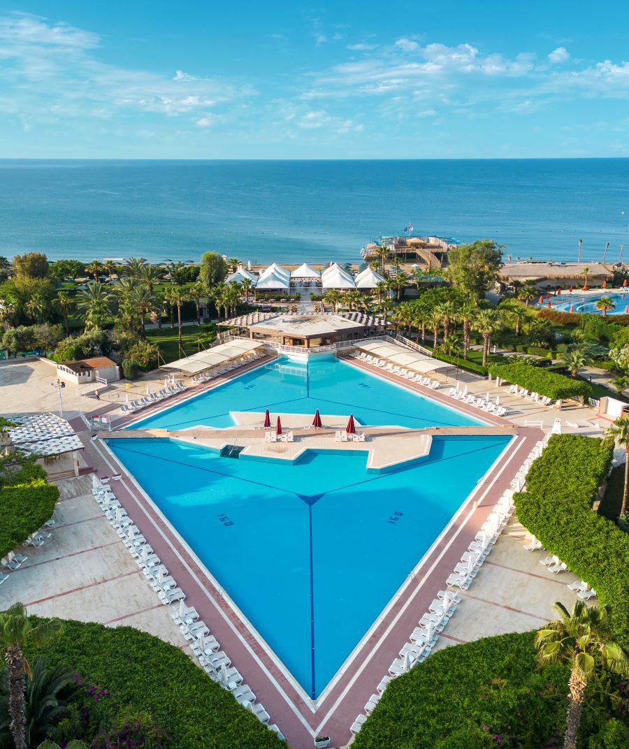 Outdoor swimming pool with sea in the distance at Kaya Belek Hotel
