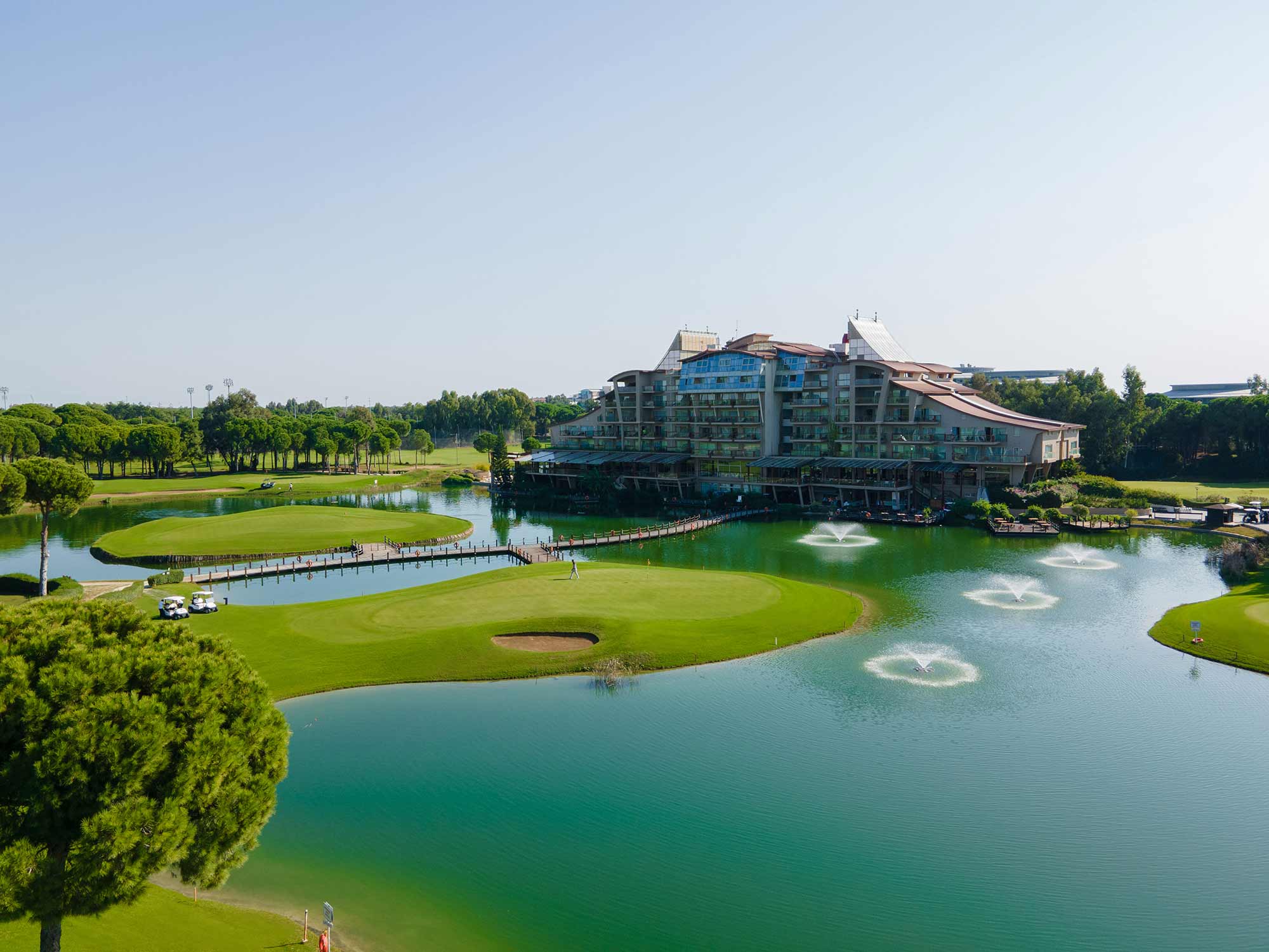 Sueno Golf Hotel Belek from the air with the lake and bridge surrounding the golf course in the foreground