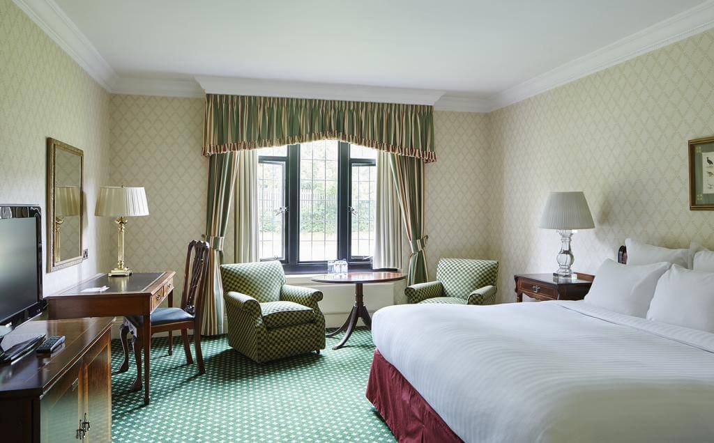 Double bedroom with desk, chair, armchairs and television at Hanbury Manor Golf Marriott Hotel And Country Club