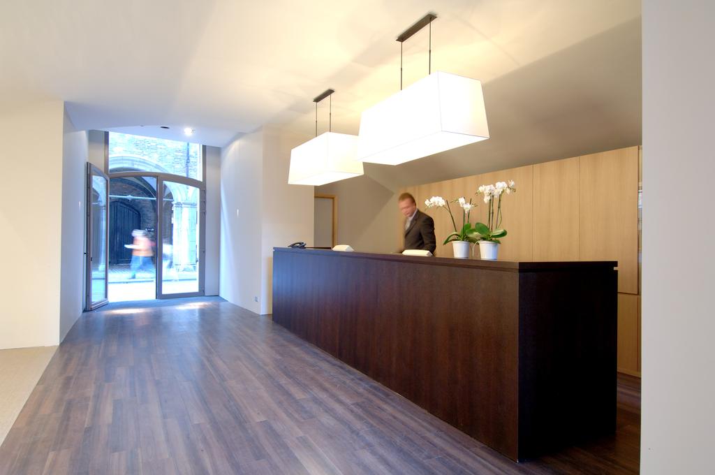 Reception desk at Martin's Hotel Brugge with wooden desk and two flowers in pots on top, and receptionist