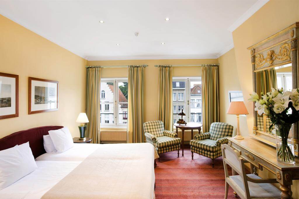 Bedroom with twin beds at Martin's Relais, along with desk, chair, mirror on the wall, green armchairs and windows looking out onto the street