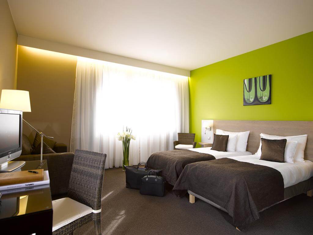 Twin bedroom at Martin's Waterloo with green wall, brown cushion and throw, desk, chair and flat screen television