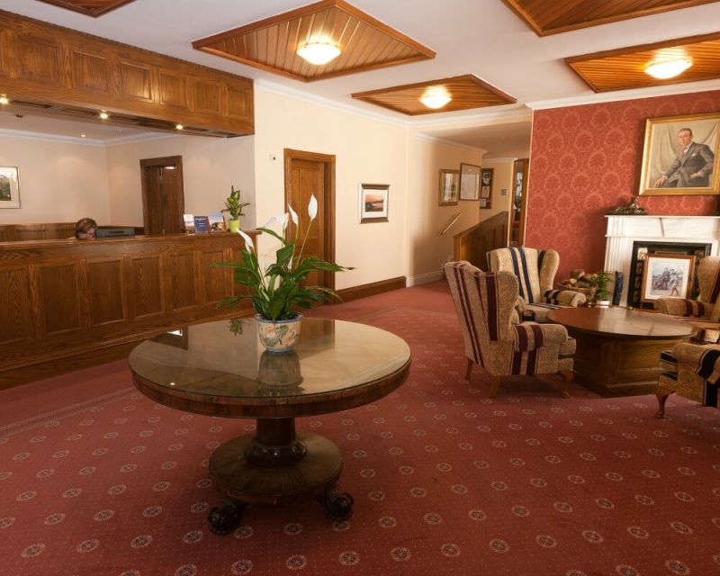 Wood panelled reception desk with wooden table and armchairs at Rosapenna Hotel And Golf Resort