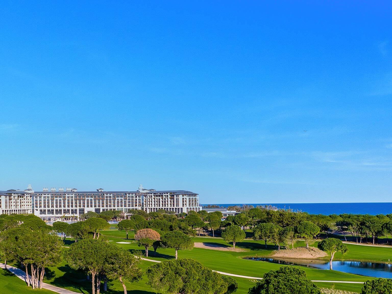Blue skies overlooking Cullinan Belek with the golf course in the foreground, surrounded by green trees