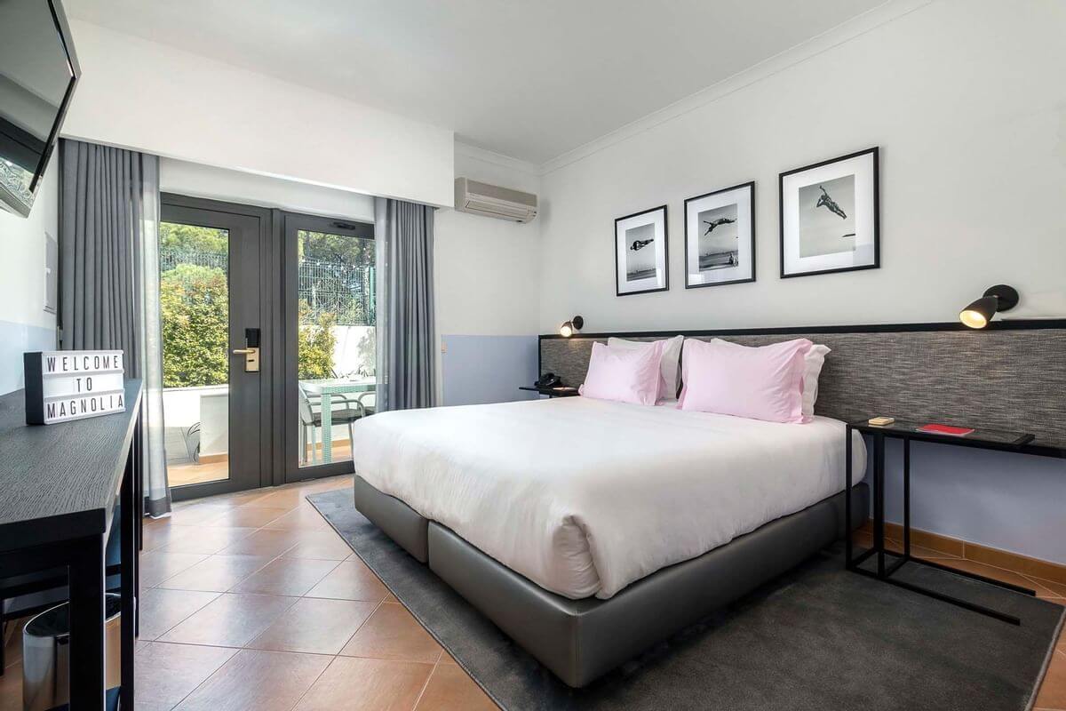 Double bedroom at The Magnolia Hotel with three pictures above the bed, flat screen television and patio doors leading to the veranda