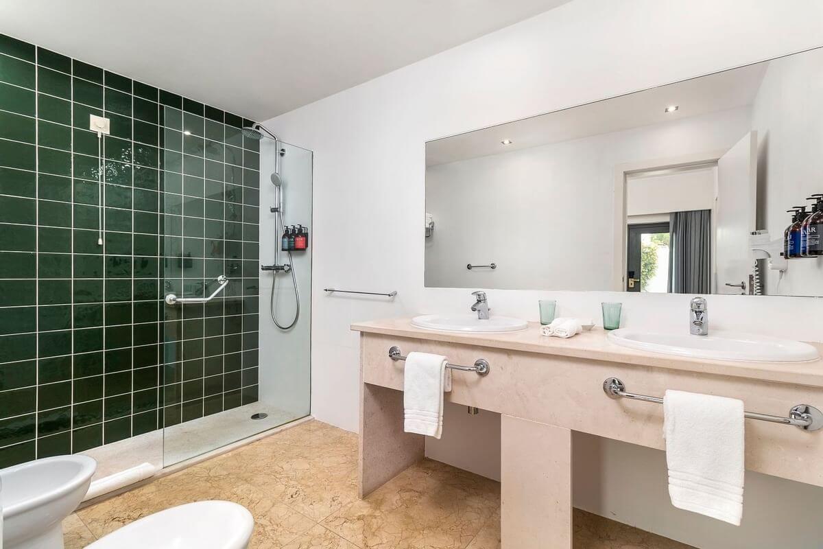 Bathroom at The Magnolia Hotel with separate shower cubible, two sinks, one mirror and toilet