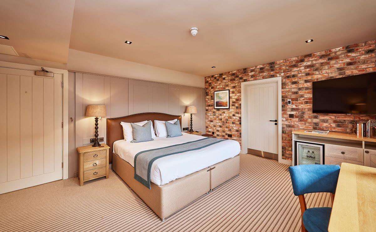 Bedroom with double bed at Sanburn Hall, with blue chair and wooden desk, and television mounted on the door