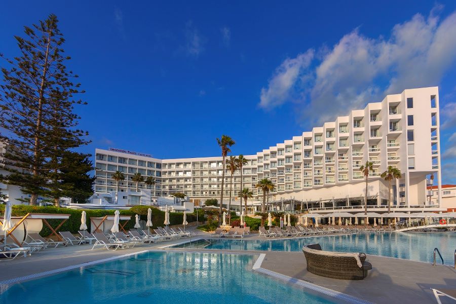 Exterior shot of Leonardo Plaza Cypria Maris Beach Hotel & Spa with swimming pool in foreground surrounded by palm trees